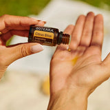 dōTERRA Belebende Mischung (Citrus Bliss) 15ml – Hände tragen Tropfen auf Handfläche auf, grünes Bokeh im Freien | doTERRA