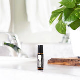 dōTERRA Copaiba Touch Roll-On 10ml – Flasche auf Badezimmertheke neben Wasserhahn und Efeutute | doTERRA