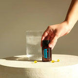 dōTERRA DDR Prime Softgels – Hand greift nach Flasche neben Wassergefäß auf Stein | doTERRA