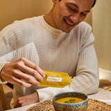 dōTERRA EO Mega Nahrungsergänzung – Mann schüttet Sachet lächelnd in Suppe | doTERRA