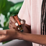 dōTERRA Neroli Touch Roll-on 10ml – Frau mit dunkler Haut wendet es am Handgelenk neben einer Pflanze an | doTERRA