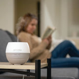 dōTERRA Petal Diffuser auf Tisch Frau lesend auf Sofa im Wohnzimmer | dōTERRA Aromatherapie