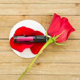 dōTERRA Rosen Touch Roll-on 10ml auf weißer Basis mit rosa-roten Rosenblättern auf Holz Aufsicht | doTERRA